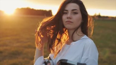 Şehvetli genç bir kız gün batımına karşı duruyor ve uzun saçlarını eliyle parmaklıyor. Yakın plan. Yavaş çekim