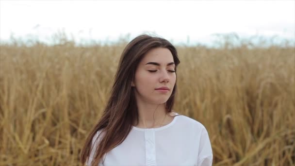 Aantrekkelijk jong meisje in witte kleren staat midden in een tarweveld en mediteert. Een close-up. Langzame beweging — Stockvideo