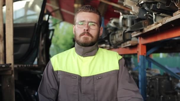 Çekici, sakallı, gözlüklü bir tamirci yedek parça raflarının önünde duruyor ve iç çekiyor. Yakın plan. Ağır çekim. Kamera uzaklaşıyor. — Stok video