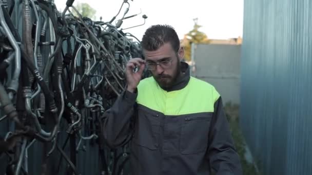 Ein junger bärtiger Mechaniker läuft an den Ersatzteilregalen eines Autoservice-Lagers vorbei und justiert seine Brille. Nahaufnahme — Stockvideo