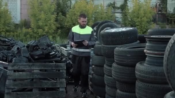 Fleißige junge bärtige Automechaniker mit Brille prüfen die gefalteten Reifen, indem sie Notizen in einem Notizbuch machen. Nahaufnahme — Stockvideo