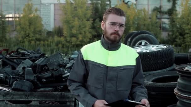 Un jeune mécanicien barbu à lunettes se tient debout sur les rangées de roues arrière-plan et parle sérieusement quelque chose à la caméra. Gros plan. Mouvement lent — Video