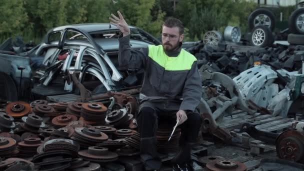 Handsome young auto mechanic in glasses smokes sitting among spare parts and and throws the cigarette butt with a mannered gesture and leaves — Stock video