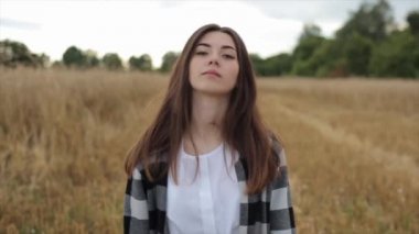 Beyaz elbiseli çekici genç kız buğday tarlasının ortasında duruyor ve meditasyon yapıyor. Yakın plan. Yavaş çekim