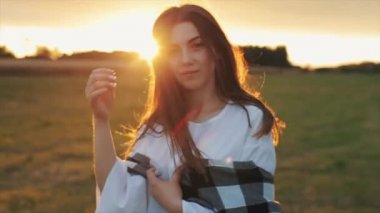 Şehvetli genç bir kız gün batımına karşı duruyor ve uzun saçlarını eliyle parmaklıyor. Yakın plan. Yavaş çekim