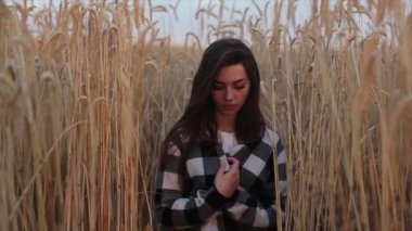 Doğanın arka planına karşı gözleri kapalı duran ve elinde buğday dikenleri tutan genç bir kız. Kaba bir plan. Yavaş çekim