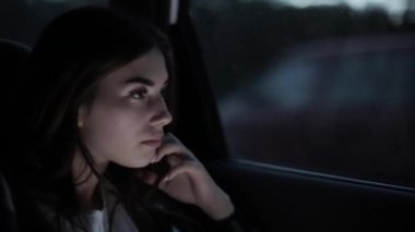 Genç bir kız arabanın camına oturur ve yüzü telefon ekranını aydınlatır. Yan görüş. Yakın plan. Bulanık arkaplan