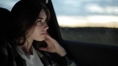 Düşünceli genç bir kız araba penceresinden gün batımına hayran. Yakın plan. Yan görüş. Yavaş çekim
