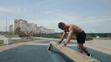 Çıplak gövdeli genç kaslı adam spor sahasında egzersiz yapıyor ve spor kirişinde amuda kalkıyor. Yan görünüm