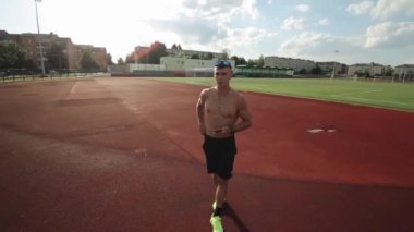 Çıplak gövdeli genç kaslı bir adam elinde telefonla stadyumda yürür ve kameraya konuşur. Kamera yakınlaşıyor ve uzaklaşıyor.