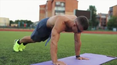 Spor şortlu kaslı bir adam futbol sahasında antrenman yapıyor ve kol ve bacak kasları üzerinde egzersiz yapıyor. Yan görüş. Yakın plan.