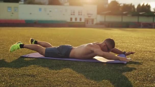 一名身披蓝色短裤的健美运动员在体育场接受训练，并在阳光灿烂的天空下跳跃和俯卧撑。特写。侧视图 — 图库视频影像