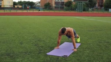 Şehir stadyumunda vücut geliştirme eğitimi alan ve elleri spor minderinin üzerinde zıplayan bir adam. Ön manzara. Yakın plan. Arka plan bulanık. Sporcu eğitim için telefonunda mobil uygulama kullanıyor.
