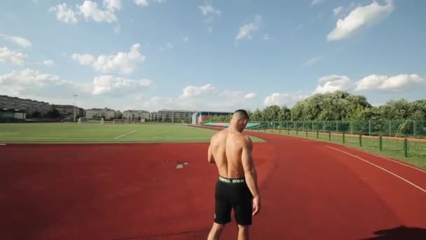 Misk, Bielorrusia - 25 de agosto de 2020: Un joven musculoso en pantalones cortos deportivos camina por el estadio de la ciudad con un teléfono en la mano. Rotación en torno al tema — Vídeo de stock