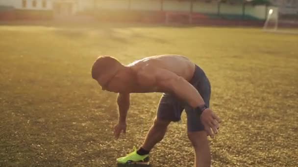 Egy kék rövidnadrágos testépítő edz a stadionban, és ugrál és fekvőtámaszt készít a napos égbolt hátterében. Közelkép. Oldalnézet — Stock videók