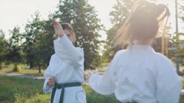 Doğada karate antrenmanı yapan iki genç kadın dövüş sanatları eğitimi alıyor. Yakın plan. Ağır çekim. Kamera sporcuların hareketlerini izliyor.