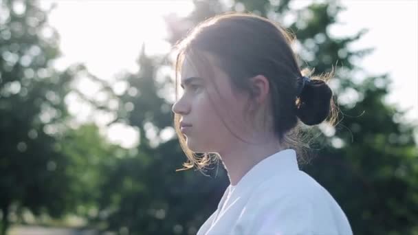 Portrait d'une jeune fille de profil debout sur un fond d'arbres par une journée ensoleillée d'été. Gros plan. Au ralenti. Fond flou — Video