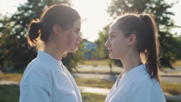 Dos atletas femeninas en el entrenamiento de karate participan en una batalla de puntos de vista y se ríen en voz alta. Vista lateral. Primer plano. Fondo borroso — Vídeo de stock