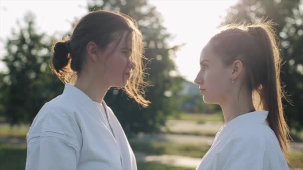 Gezichtsstrijd. Twee jonge meisjes in karate klassen kijken elkaar in de ogen en een van hen kijkt weg. Zijaanzicht. Een close-up. Langzame beweging — Stockvideo