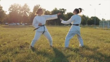 Açık havada karate eğitimi alan iki genç kadın savunma ve saldırı tekniğini uyguluyor. Yakın plan. Ağır çekim. Bulanık arkaplan