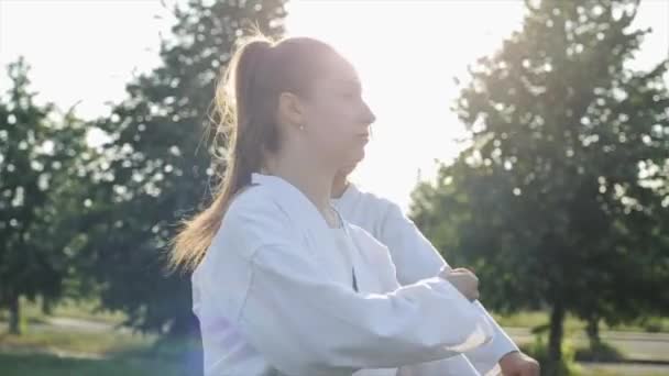 Junge Frauen in weißen Kimonos trainieren vor dem Hintergrund der Natur und feilen an ihren Karate-Fähigkeiten. Seitenansicht. Nahaufnahme. Zeitlupe — Stockvideo
