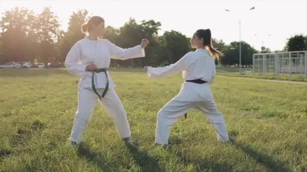 Two female athletes in white kimonos are holding a demonstration fight during karate training outdoors. Close-up — Stock Video