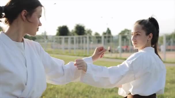 Jonge vrouwen zijn bezig met sparringkaratetraining op de achtergrond van het sportveld. Een close-up. Wazige achtergrond — Stockvideo