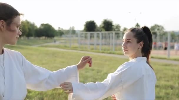 Venkovní trénink karate. Mladá dívka provádí techniku bojového umění a strká svého sparring partnera na zem. Detailní záběr. Rozmazané pozadí — Stock video