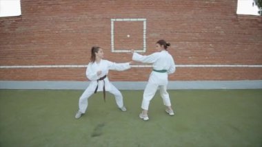 Karate antrenmanında olan iki genç kadın duvara yumruk atıp tekmeliyor. Yakın plan. Kamera yakınlaşır ve uzaklaşır