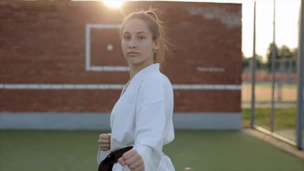 Młoda kobieta jest zaangażowana w karate na boisku sportowym i krzyczy agresywnie demonstrując technikę. Z przodu. Zbliżenie. Zwolniony ruch — Wideo stockowe