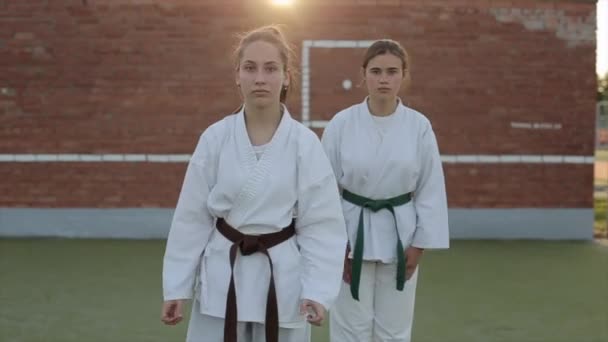 Młode dziewczyny w białych kimonach kłaniają się i pokazują różne techniki karate podczas ćwiczeń na boisku. Z przodu. Zbliżenie. Zwolniony ruch — Wideo stockowe