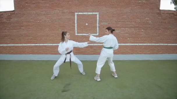 Two young women in karate training practice punches and kicks in pair against the background of a brick wall. Close-up. Camera zooms in and out — Stock Video