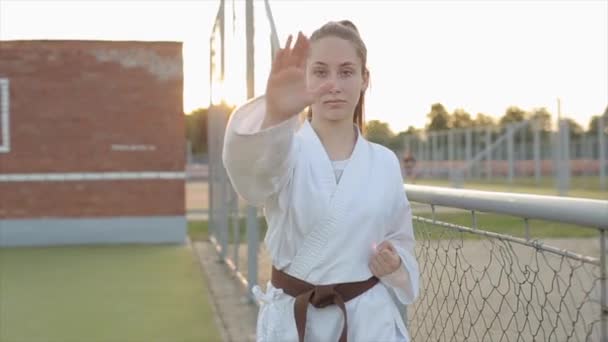 Dziewczyna karate ćwicząca na boisku sportowym demonstruje ruch rąk przy użyciu techniki Kyokushinkai. Z przodu. Zbliżenie. Zwolniony ruch — Wideo stockowe