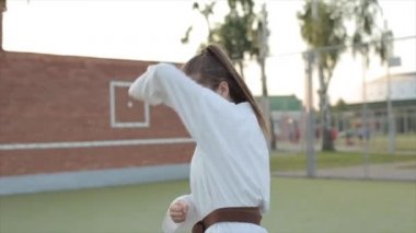 Kahverengi kuşaklı beyaz kimonolu bir bayan sporcu gün batımının arka planında karate teknikleri gösteriyor. Yakın plan. Ön görünüm