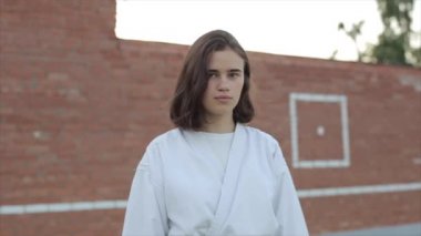 Duvarın arkasında duran beyaz kimonolu genç bir karateci kızın portresi. Ağır çekim. Bulanık arkaplan