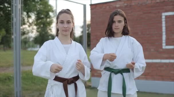 Mladé dívky v bílých kimonech předvádějí základní postoj karate na sportovním hřišti. Přední pohled. Detailní záběr. Zpomalený pohyb — Stock video