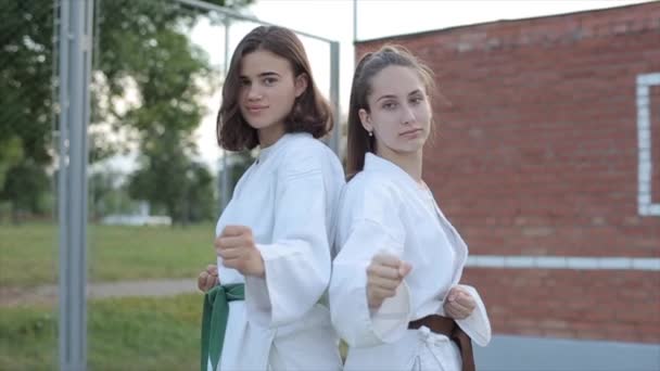 Dwie atletki wykazują podstawową postawę karate stojąc plecami do siebie. Z przodu. Zbliżenie. Kamera robi zbliżenie. Zwolniony ruch — Wideo stockowe