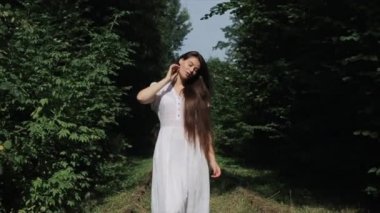 Şehvetli genç bir kadın ormanda yeşil ağaçların arasında yol boyunca yürüyor ve uzun saçlarını eliyle düzleştiriyor. Yakın plan. Ön manzara. Yavaş çekim