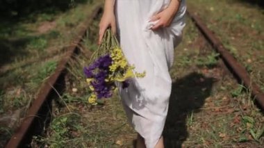Beyaz elbiseli çekici bir genç kız eski demiryolunun yatağında çıplak ayakla yürüyor ve elinde çiçekler tutuyor. Yakın plan. Ağır çekim. Kamera aşağıdan yukarıya hareket eder