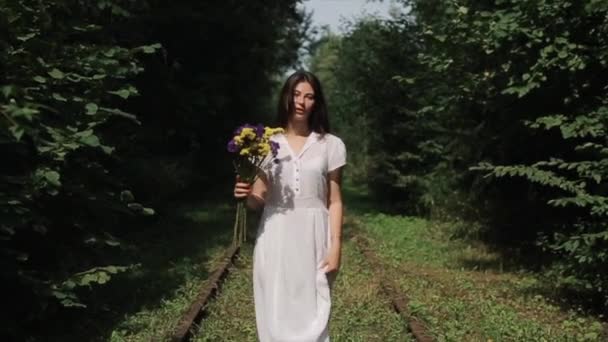 ベラルーシの平和的な抗議行動で暴力と残酷さに対する彼女の手の中に白いドレスと花の美しい若い女性は、緑の木を背景に歩いています。スローモーション — ストック動画