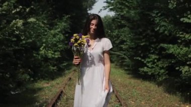 Beyaz elbiseli, elinde çiçeklerle Belarus 'taki barışçıl protestolarda şiddete ve zulme karşı duran güzel bir genç kadın yeşil ağaçların arka planında yürüyor. Yavaş çekim