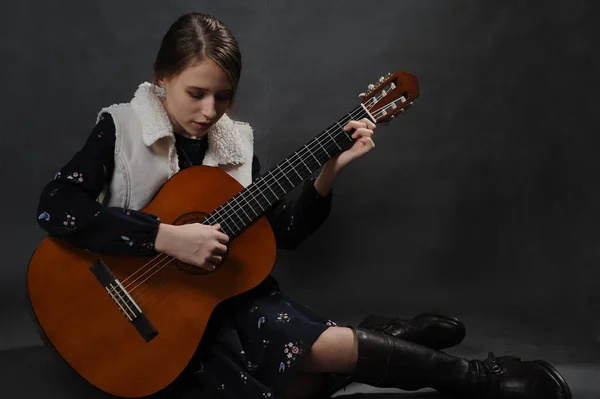 Girl play guitar. Studio light. Dark background.