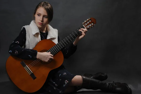 Girl play guitar. Studio light. Dark background.