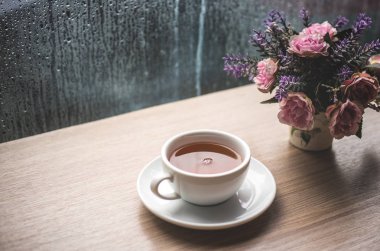 Limonlu yeşil çay damla su yağmur sezonu ile ahşap masa üzerinde beyaz bir fincan. kafeterya salonu ile tencerede gül çiçek