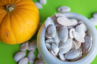 Yeşil bir masada beyaz bir kasede kurumuş kabak tohumları, seçici bir odak noktası..