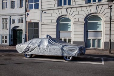 parked car covered with tent on empty street with historical buildings in copenhagen, denmark clipart