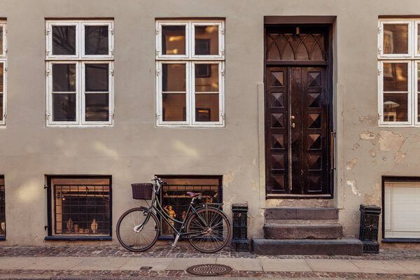 parked bicycle with basket near grey building with closed doors on street in copenhagen, denmark