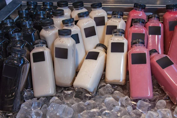 Close up view of various types of bottles with smoothies in refrigerator with ice cubes — Stock Photo