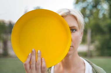 beautiful blonde woman holding yellow flying disk and looking at camera clipart
