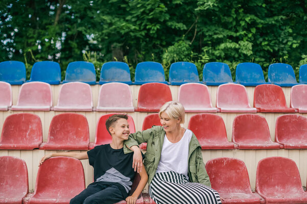 happy mother and son smiling each other while sitting together on stadium seats